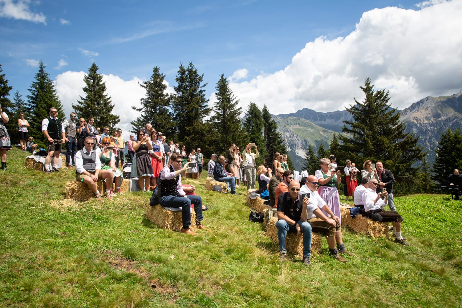 Hochzeitsgesellschaft bei einer Alphochzeit in Lenzerheide, die das Ankommen der Braut verfolgt, fotografiert von Hochzeitsfotograf Adrian Flütsch.