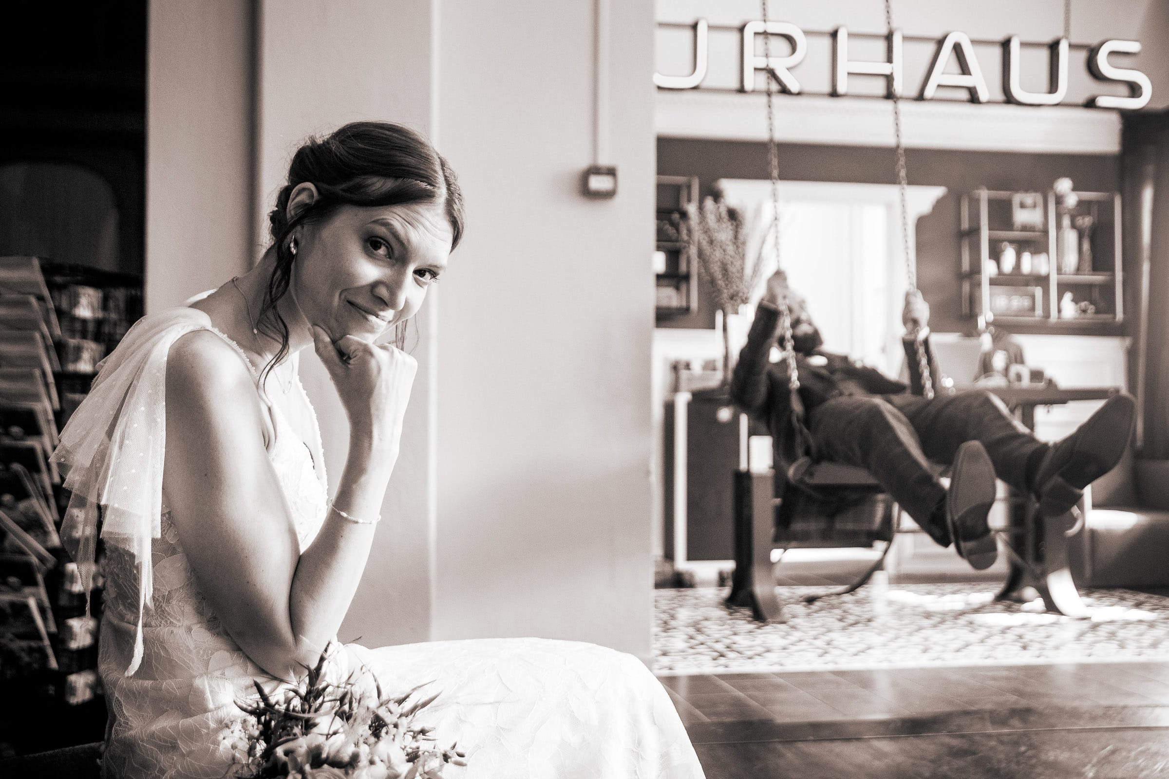 Braut mit verschmitztem Lächeln und Bräutigam auf einer Schaukel – humorvolles Hochzeitsfoto von Fotograf Adrian Flütsch, aufgenommen im Hotel Kurhaus in Lenzerheide. Traumhochzeitsbilder steht für Hochzeitsfotografie, die Herzen berührt.