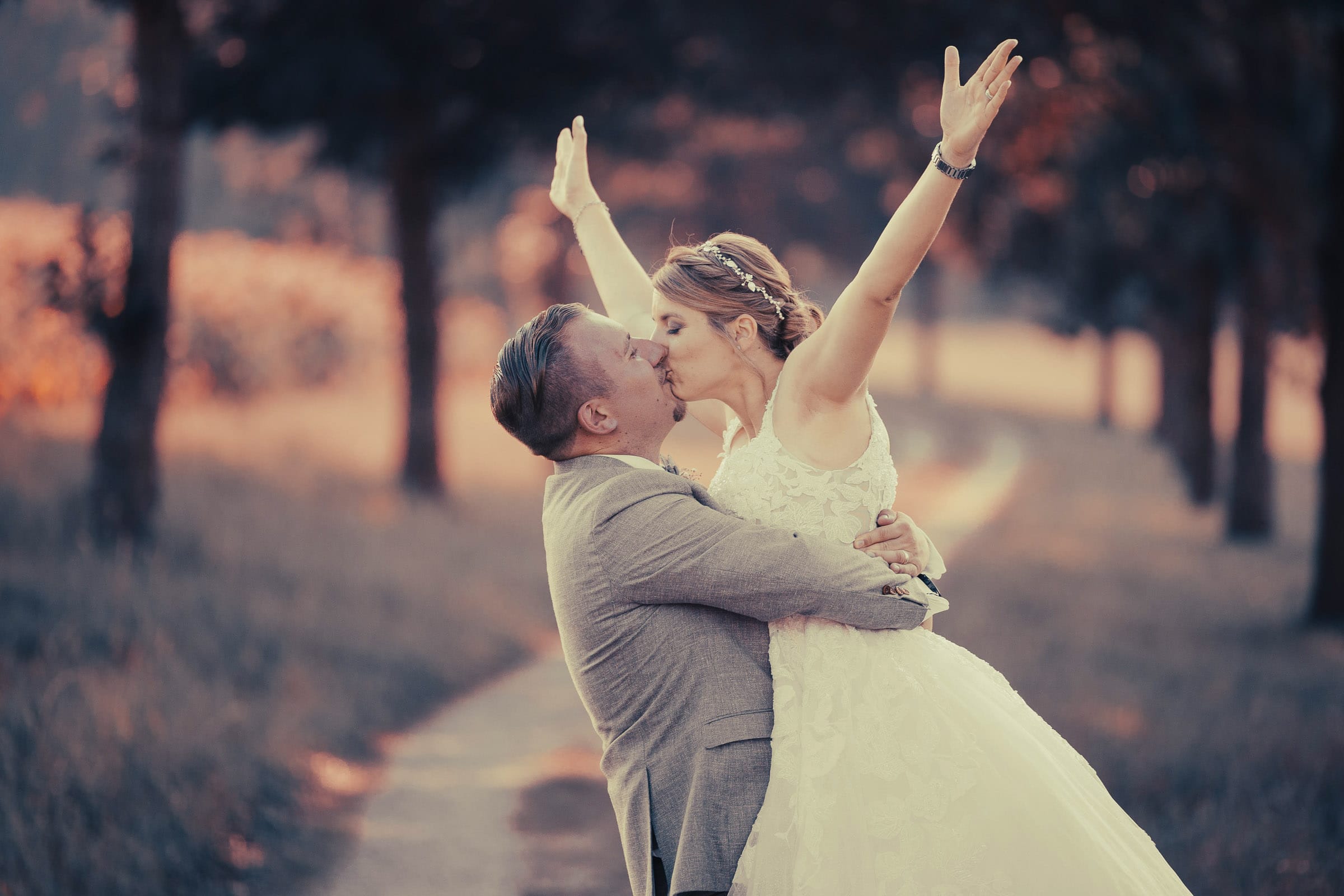 Glückliches Brautpaar beim Kuss in romantischer Abenddämmerung auf einem idyllischen Weg